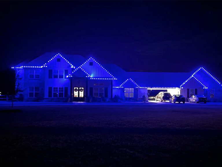 Large College Station home with blue holiday lights installed on the front of the house. The front of the house is glowing blue.