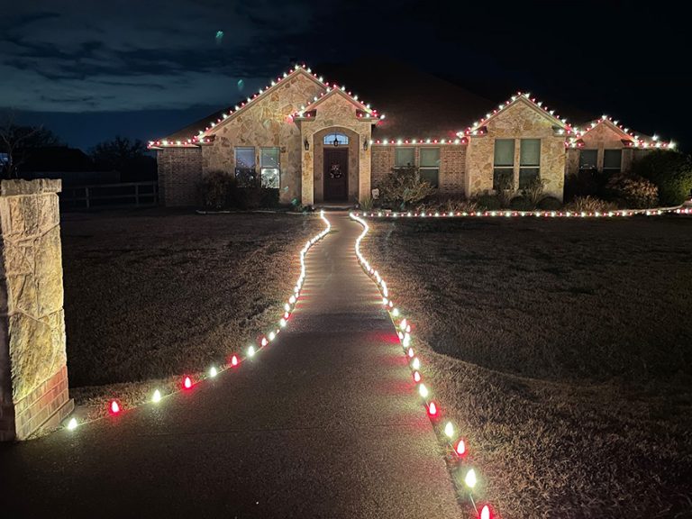 Home with professional Christmas lights in Leander Texas. Red and white lights line the pathway to the front of the house and roof line.