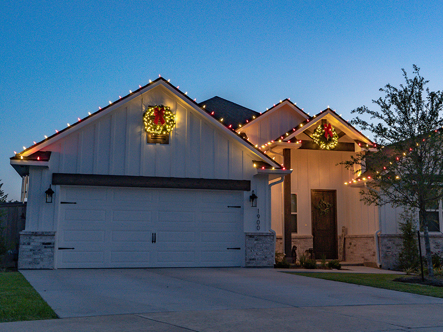 House with xmas lights installed on the roof and Christmas wreaths with lights over the garage and front door