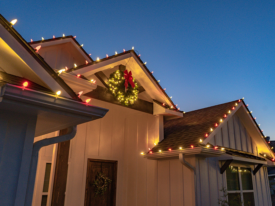 Front entry of a farmhouse style home with Christmas lights and a wreath wrapped in lights with a bow over the front door