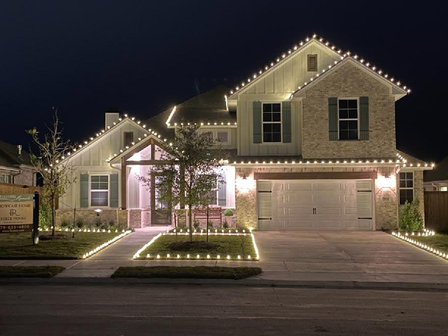 Two story house with white outdoor Christmas lights on the roof and around the yard.