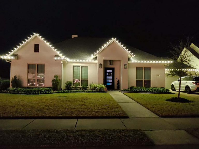 Christmas lights professionally installed on a new home. The lights are white and line the roof of the white brick house.