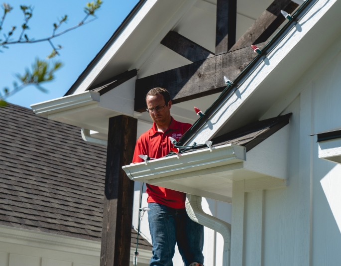 A professional Christmas light installer from Texas Light Crew installing red and white Christmas lights on the roofline of a home in the Brazos Valley.