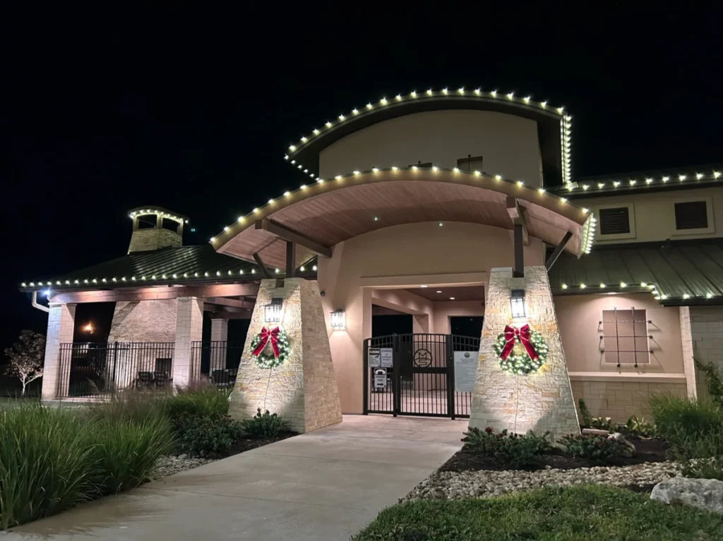 Front entrance of a business lined with Christmas lights, wreaths on pillars on each side of the door