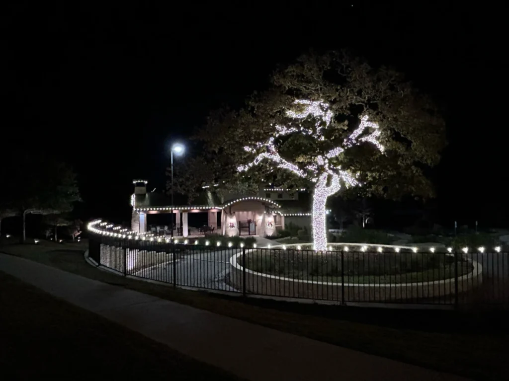 Tree, fence and building lined with Christmas lights