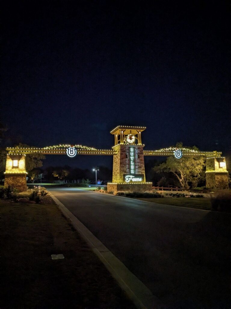 Neighborhood entrance archway and stone tower outlined in warm white lights with wreaths and garland