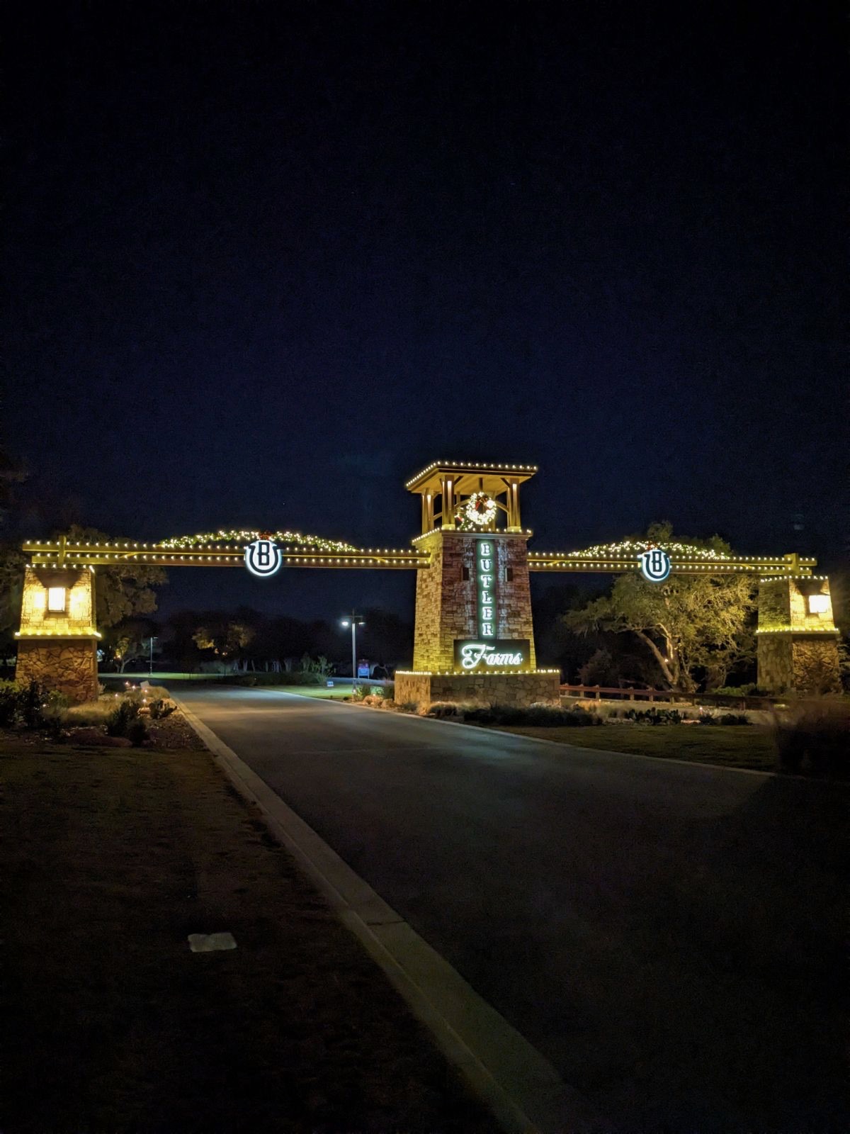 Neighborhood entrance archway and stone tower outlined in warm white lights with wreaths and garland