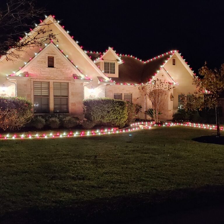 Stone home with red and white C9 Christmas lights on every roofline and along the landscape beds