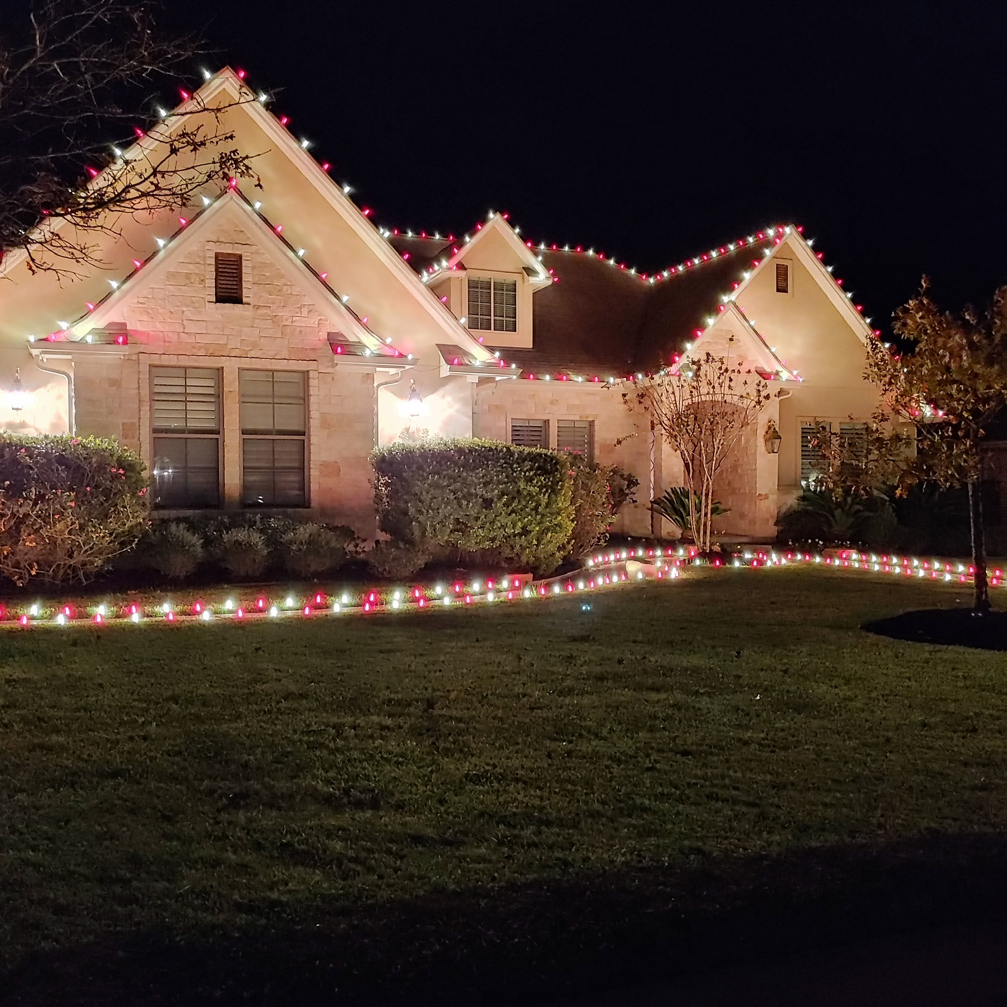 Stone home with red and white C9 Christmas lights on every roofline and along the landscape beds