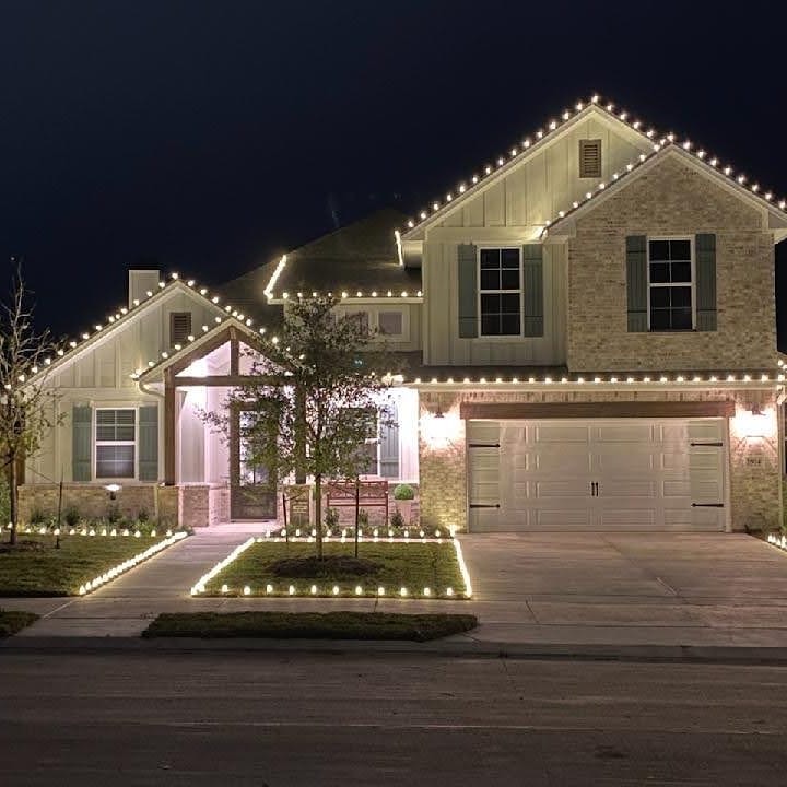 Two-story home with warm white Christmas lights on the roofline, windows, and landscaping