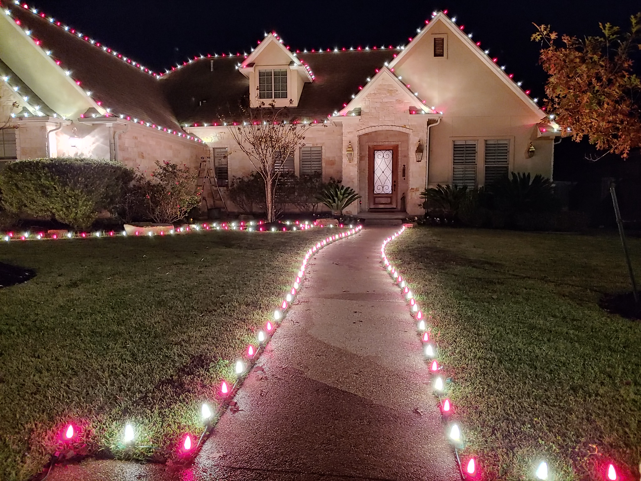 Home with red and white Christmas lights on the roofline and C9 bulbs lining the front walkway