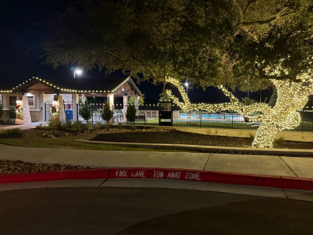 Neighborhood pool pavilion with roofline lights and a large oak tree wrapped in warm white lights