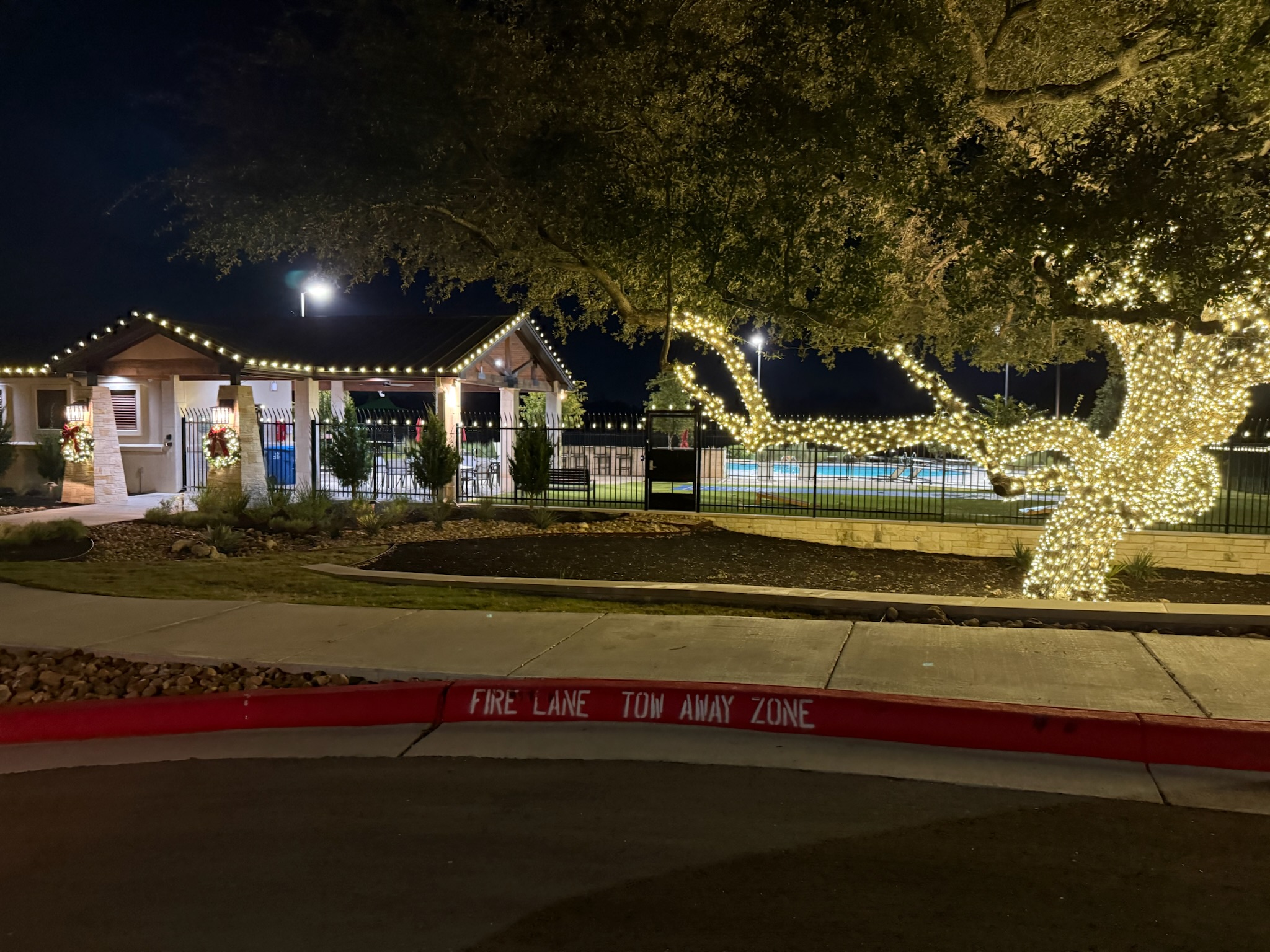 Neighborhood pool pavilion with roofline lights and a large oak tree wrapped in warm white lights